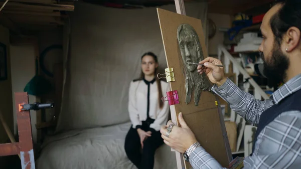 Скульптор створює скульптуру людей обличчям на полотні, а молода жінка позує його в художній студії — стокове фото