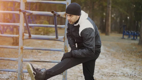Atractivo corredor hombre haciendo ejercicio de estiramiento preparándose para el entrenamiento de la mañana y trotar en el parque de invierno — Foto de Stock