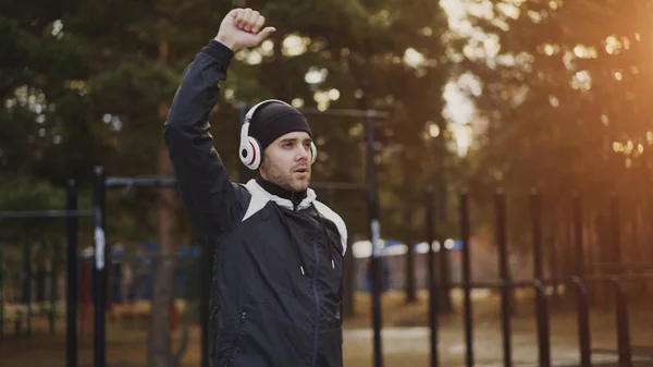 Hombre guapo en auriculares haciendo ejercicio de estiramiento mientras escucha música en el parque de invierno — Foto de Stock