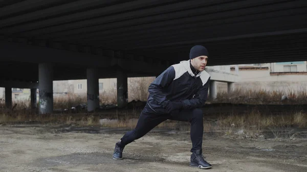 Aantrekkelijke man runner stretching oefening voor ochtend training te doen en te joggen op stedelijke locatie buiten in de winter — Stockfoto