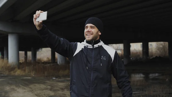 Hombre deportivo feliz tomando retrato selfie con teléfono inteligente después de entrenar en la ubicación urbana al aire libre en invierno —  Fotos de Stock