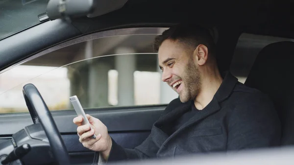 Vonzó üzletember nevetve, miközben használ smartphone utazás után kocsiban ül — Stock Fotó