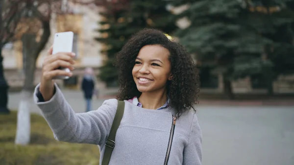 Vidám kevert diák lány beszél a videohívás smartphone közelében univercity — Stock Fotó