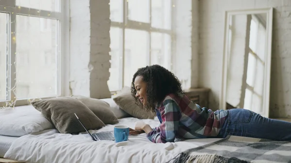 Attraktive Teenie-Mädchen mit gemischter Rasse lachen mit Laptop, um soziale Medien zu teilen, die zu Hause im Bett liegen — Stockfoto