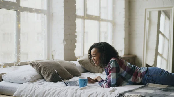 Attraktive Teenie-Mädchen mit gemischter Rasse lachen mit Laptop, um soziale Medien zu teilen, die zu Hause im Bett liegen — Stockfoto