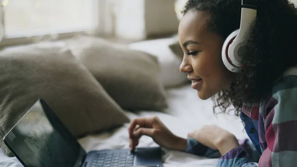 Nahaufnahme von afrikanisch-amerikanischen Mädchen Musik hören, während sie Fotos online auf Laptop auf dem Bett liegend ansehen — Stockfoto