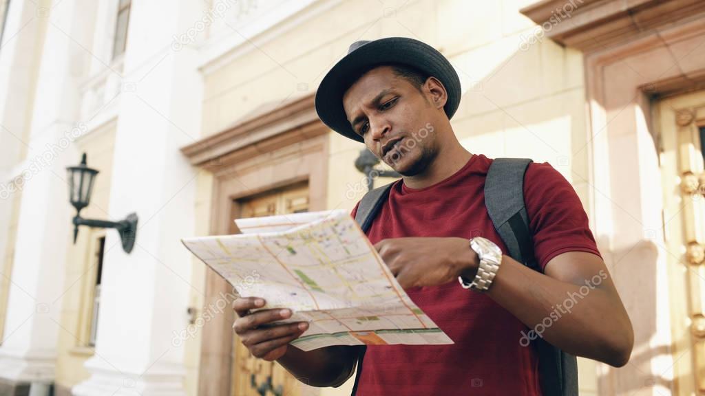 African american tourist man looking into paper city map exploring sightseeings during travelling in Europe