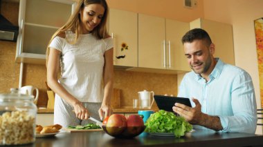 Sabah mutfakta sohbet çekici çift. Yakışıklı adam kız arkadaşı yemek yaparken tablet kullanma