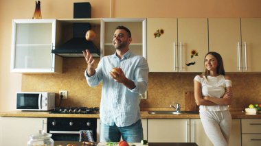 Çekici sevgi dolu çift mutfakta eğleniyor. Yakışıklı bir adam kız arkadaşını etkilemek için elma ile hokkabazlık