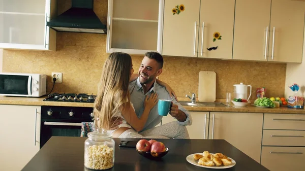 Привлекательная молодая пара обнимается рано утром на кухне, пока мужчина завтракает — стоковое фото