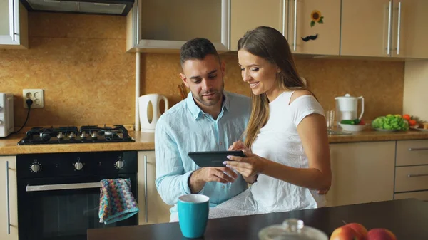 Щаслива молода пара використовує цифровий планшетний комп'ютер, сидячи на кухні і снідаючи вранці — стокове фото