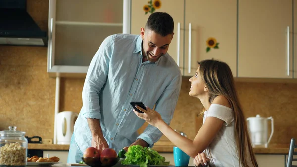 Attraktives Paar frühmorgens in der Küche. schönes Mädchen teilt soziale Medien auf dem Smartphone mit ihrem Freund — Stockfoto