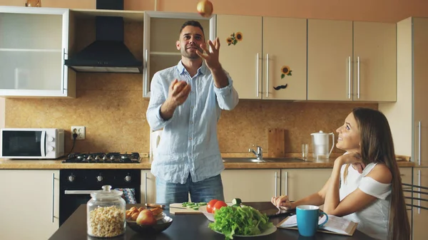 Приваблива любляча пара розважається на кухні. Красивий чоловік жонглює з яблуками, щоб справити враження на свою дівчину — стокове фото
