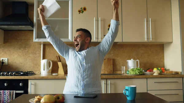 Bel homme Recevoir de bonnes nouvelles lettre de lecture dans la cuisine tandis que prendre le petit déjeuner à la maison tôt le matin — Photo