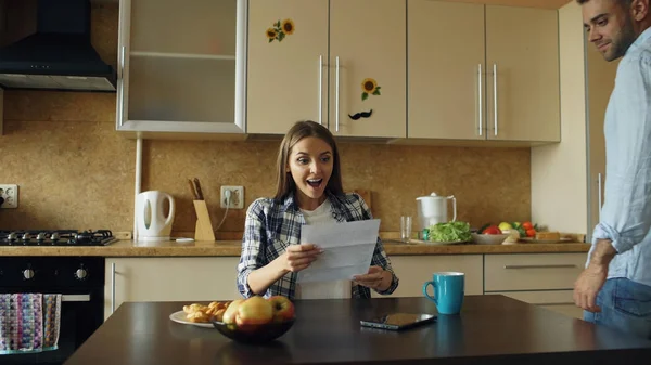 Приваблива щаслива пара отримує хороші новини, що розгортаються лист на кухні під час сніданку вдома — стокове фото