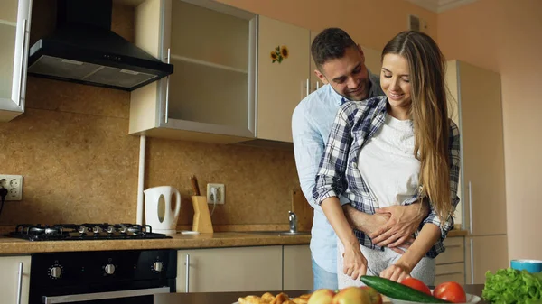 Feliz pareja joven abrazando y hablando en la cocina mientras se cocina el desayuno en casa — Foto de Stock