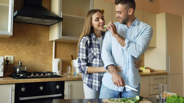 Feliz joven pareja besándose abrazando y charlando en la cocina mientras se cocina el desayuno en casa — Foto de Stock