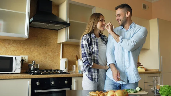 Feliz pareja joven en la cocina. Hombre guapo conocer y alimentar a su novia por la mañana temprano — Foto de Stock