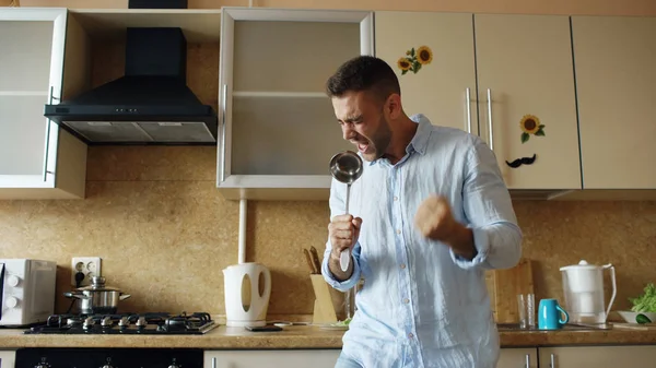 Atraente jovem engraçado homem dançando e cantando com concha enquanto cozinha na cozinha em casa — Fotografia de Stock