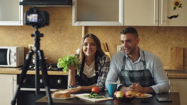 Молодая привлекательная пара съемки видео питания блог о кулинарии на dslr камеры на кухне — стоковое фото
