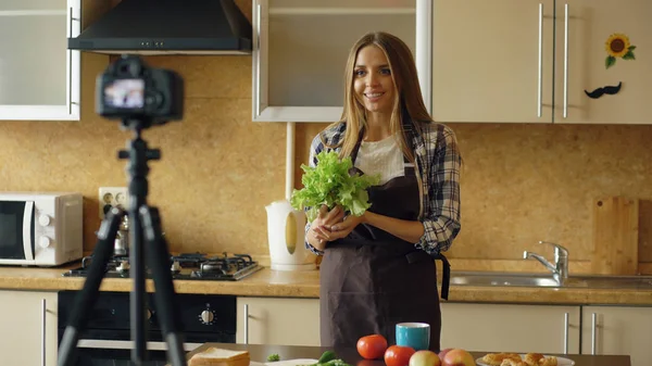 Молодая привлекательная женщина в фартуке съемки видео питание блог о приготовлении пищи на dslr камеры на кухне — стоковое фото