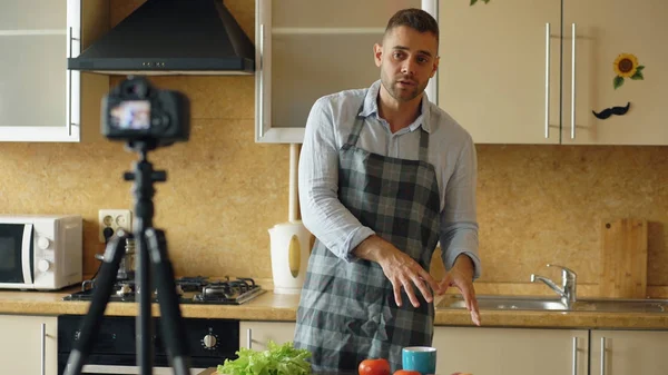 Jeune bel homme en tablier tournage vidéo blog alimentaire sur la cuisine sur caméra dslr dans la cuisine — Photo
