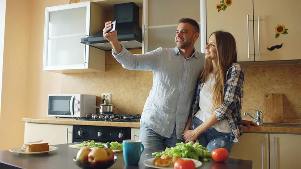 Молода щаслива пара фотографує селфі під час приготування сніданку на кухні вдома — стокове фото