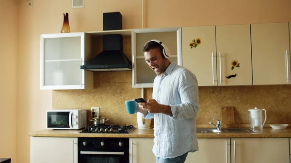 Красивий молодий смішний чоловік в навушниках танцює і співає на кухні вдома вранці і розважається у відпустці — стокове фото