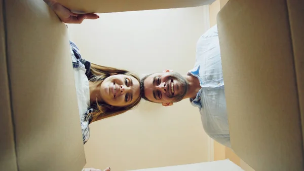 Young happy couple opening cardboard box after relocation and looking inside in new house — Stock Photo, Image