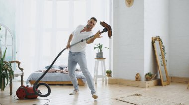 Genç adam eğleniyor dans elektrikli süpürge ile temizlik