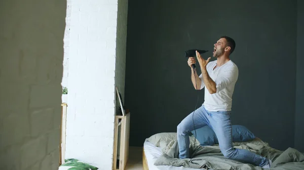 Joven cantando a secador de pelo y bailando en la cama en el dormitorio — Foto de Stock