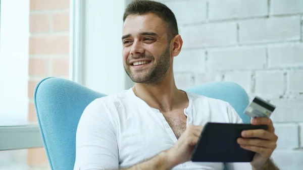 Young smiling man doing online shopping using digital tablet computer sitting at balcony at home — Stock Photo, Image