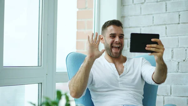 Boldog fiatalember már ül a modern tetőtéri lakás erkéllyel felszerelt digitális tábla-PC használata online videó chat — Stock Fotó
