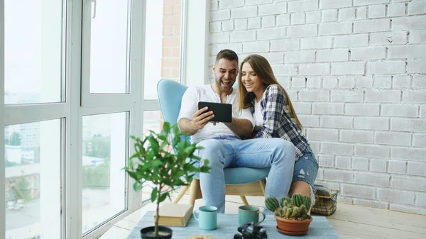Ül a modern tetőtéri lakás erkéllyel rendelkező online videó chat segítségével, a vonzó fiatal pár táblaszámítógépre — Stock Fotó