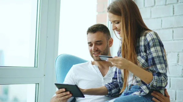 Молодая веселая пара с помощью цифрового планшетного компьютера для покупок онлайн сидеть на балконе в современной квартире лофт — стоковое фото