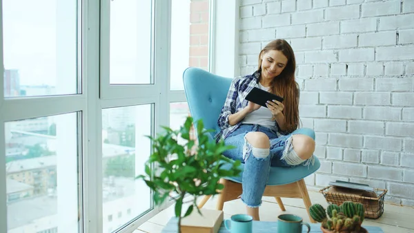 Mujer atractiva usando tableta digital sentada en la silla en el balcón en el apartamento moderno loft —  Fotos de Stock