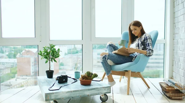 Genç çekici kadın modern loft daire balkonda oturup kitap ve içecek kahve okuyun — Stok fotoğraf