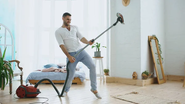 Szórakozik fiatal férfi takarítás a ház, a tánc, mint a gitáros porszívó — Stock Fotó