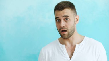 Aktif şaşırtıcı ve mavi arka plan üzerinde kameraya bakarak merak genç adam portresi