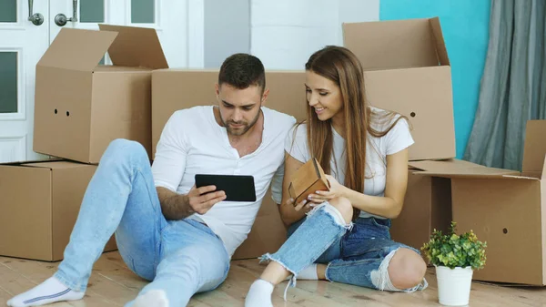 Jeune couple assis sur le sol à l'aide d'un ordinateur tablette après la réinstallation dans leur nouvelle maison — Photo