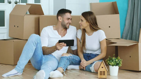 Νεαρό ζευγάρι κάθεται στο πάτωμα χρησιμοποιώντας το tablet υπολογιστή μετά τη μετεγκατάσταση στο νέο τους σπίτι — Φωτογραφία Αρχείου