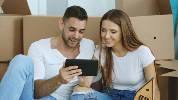 Pareja joven sentada en el suelo usando tableta después de la reubicación en su nuevo hogar — Foto de Stock