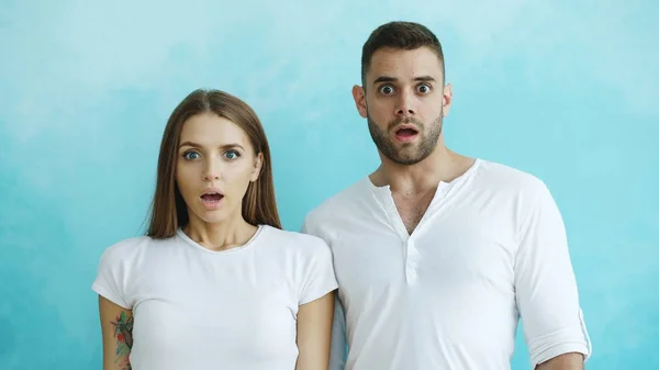 Portrait of young couple actively surprising and wondering looking into camera on blue background — Stock Photo, Image