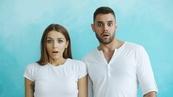 Portrait of young couple actively surprising and wondering looking into camera on blue background — Stock Photo, Image