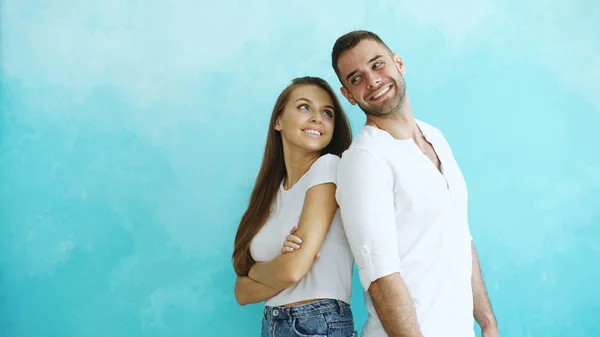 Jovem casal de pé de volta para trás flertando uns aos outros no fundo azul — Fotografia de Stock