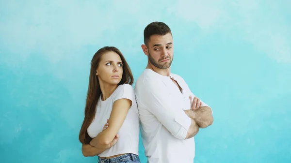 Young couple upset and angry each other standing rear on blue background — Stock Photo, Image