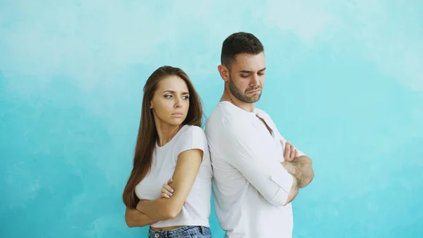 Pasangan muda marah dan marah satu sama lain berdiri belakang di latar belakang biru — Stok Foto
