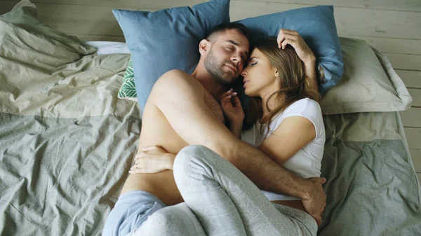 Pasangan muda yang cantik dan penuh kasih berciuman di tempat tidur di pagi hari — Stok Foto