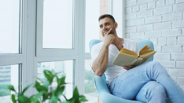 Молодий чоловік читає книгу, сидячи на балконі в сучасній квартирі — стокове фото