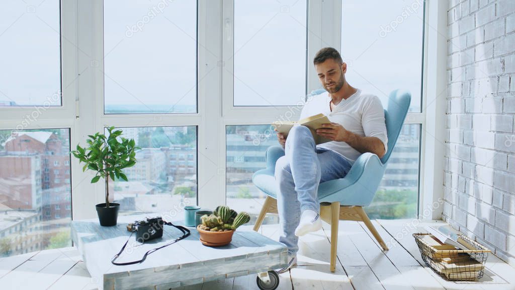 Young man read book sitting on balcony in modern apartment